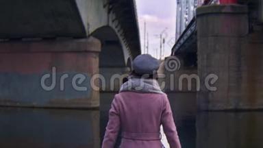女人在桥下水中行走。 库存录像。 在旧桥下行走的迷人年轻女子的后景